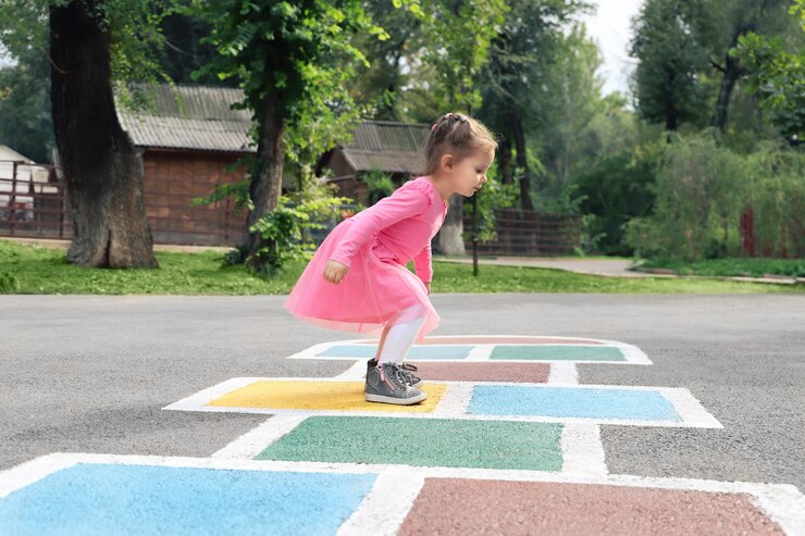 La bambina in un vestito rosa gioca a campana per strada.