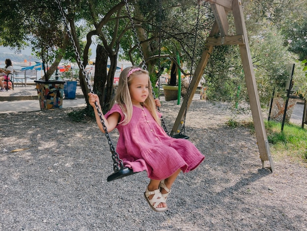 La bambina in un vestito rosa oscilla su un'altalena a catena nel parco