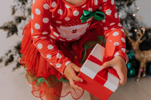 la bambina in un vestito rosso tiene un regalo di Natale nel suo primo piano delle mani