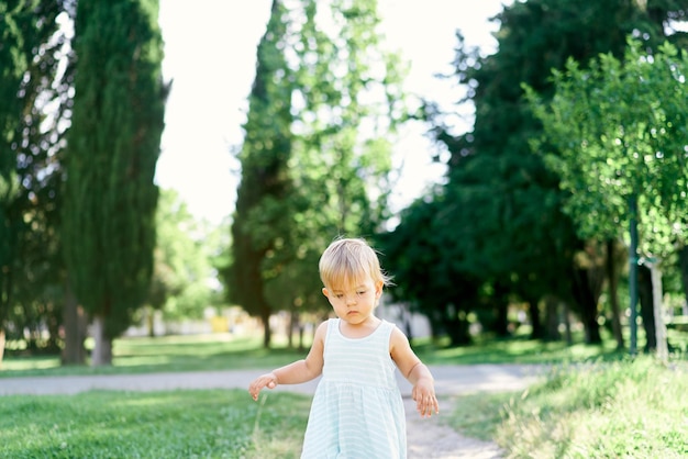 La bambina in un vestito si trova su un sentiero in un parco