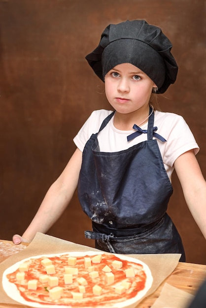 La bambina in uniforme prepara la pizza in cucina