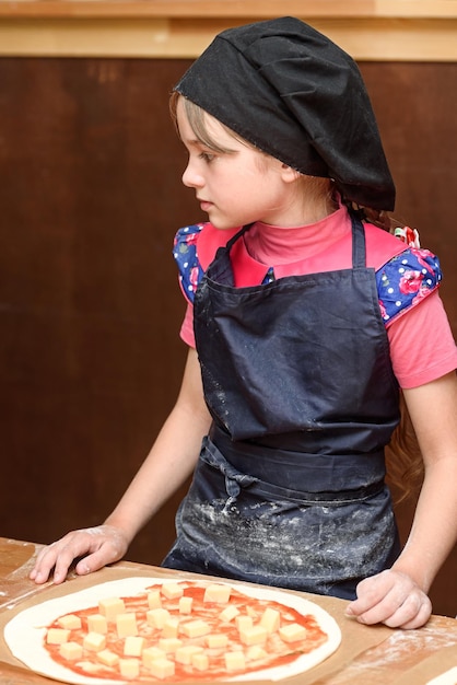 La bambina in uniforme prepara la pizza in cucina