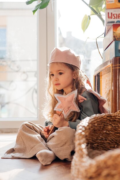 La bambina indossa ali rosa una corona una bacchetta magica e si immagina una fata magica e gioca a giochi immaginari a casa