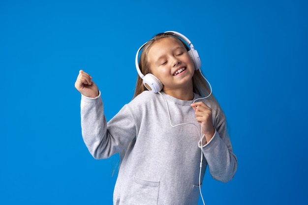 La bambina indossa le cuffie per ascoltare la musica su sfondo blu