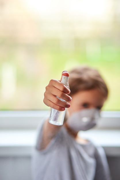 La bambina indossa una maschera igienica e preme lo spray alcolico per proteggere, disinfettare.