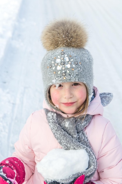 La bambina invernale tiene la neve nelle sue mani divertente