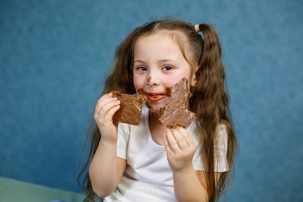 La bambina mangia cioccolato e si macchia la maglietta bianca, il viso e gli porge la mano