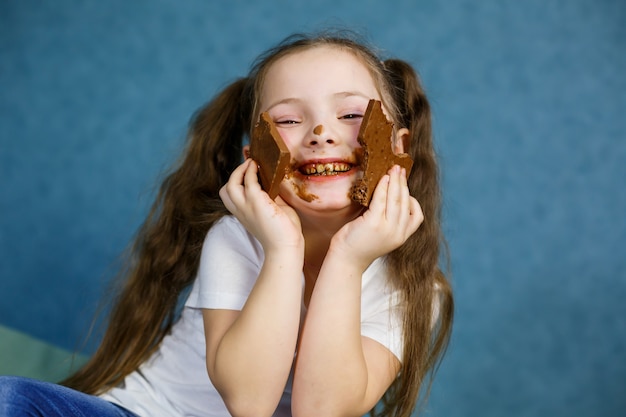 La bambina mangia cioccolato e si macchia la maglietta bianca, il viso e gli porge la mano