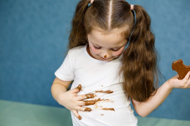 La bambina mangia cioccolato e si macchia la maglietta bianca, il viso e gli porge la mano