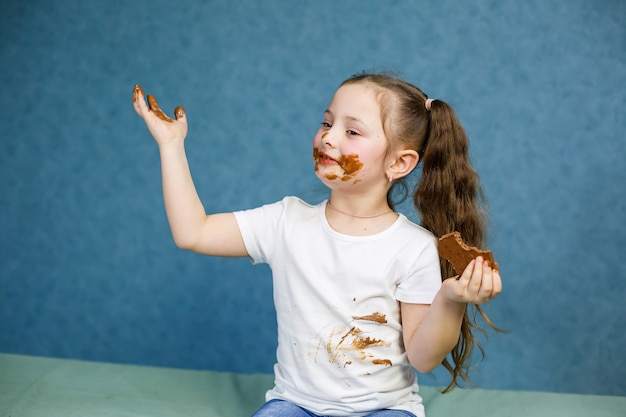 La bambina mangia cioccolato e si macchia la maglietta bianca, il viso e gli porge la mano