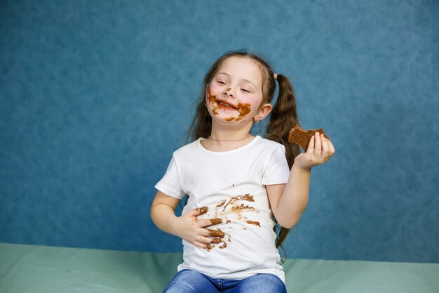 La bambina mangia cioccolato e si macchia la maglietta bianca, il viso e gli porge la mano