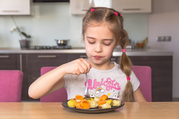 La bambina mangia pelmeni colorato.