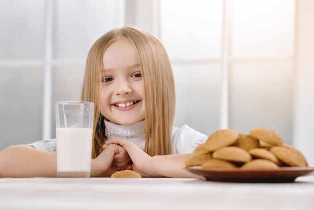 La bambina meravigliosa con il sorriso sveglio si siede vicino ai biscotti