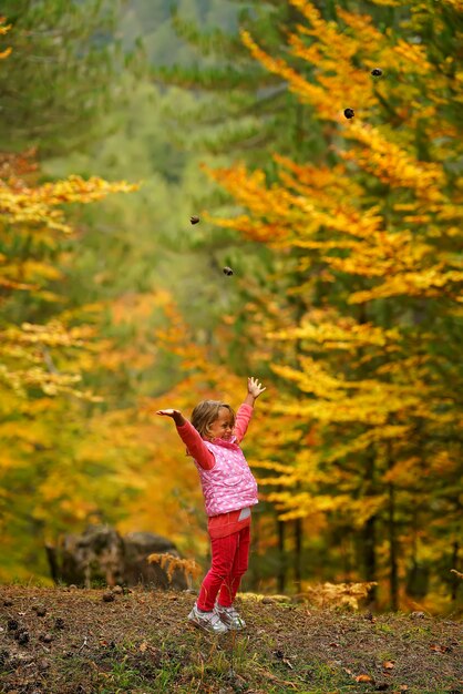 La bambina nella foresta di autunno getta sui coni