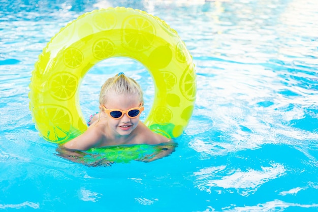 La bambina nuota in piscina con un cerchio giallo gonfiabile in estate il concetto di viaggio e svago e sorride con gli occhiali da sole