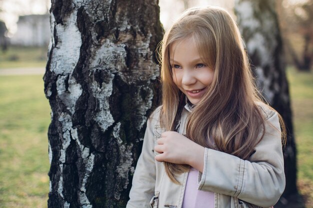 La bambina pensierosa nel parco, accanto a un albero guarda in lontananza.