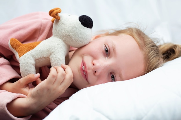 La bambina piange nel letto e abbraccia un giocattolo