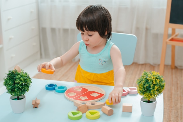 La bambina raccoglie una piramide di legno non dipinta. Giocattoli per bambini in legno naturale sicuri.