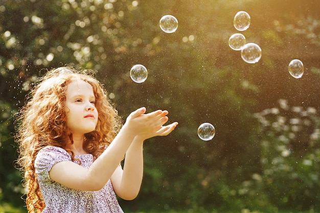 La bambina riccia cattura le bolle di sapone.