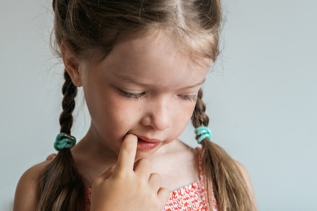 La bambina rosicchia le unghie, tenendo le dita in bocca, cattive abitudini dei bambini, concetto.