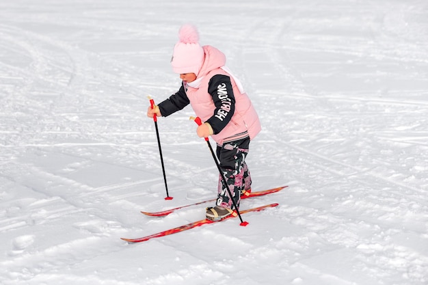 La bambina scia bambino in tuta calda rosa impara a sciare su strada innevata paesaggio invernale sno...