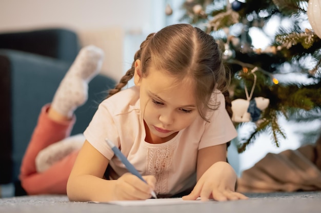 La bambina scrive la lettera Babbo Natale e sogna uno sfondo regalo Albero di Capodanno al chiuso. Buon Natale e Buone Feste.