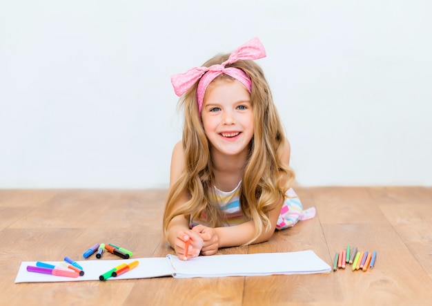 La bambina sdraiata sul pavimento disegna con le matite