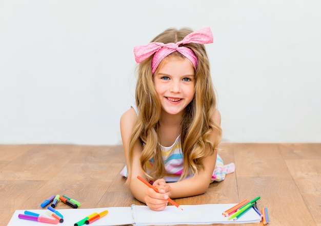 La bambina sdraiata sul pavimento disegna con le matite