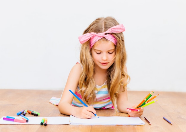 La bambina sdraiata sul pavimento disegna con le matite