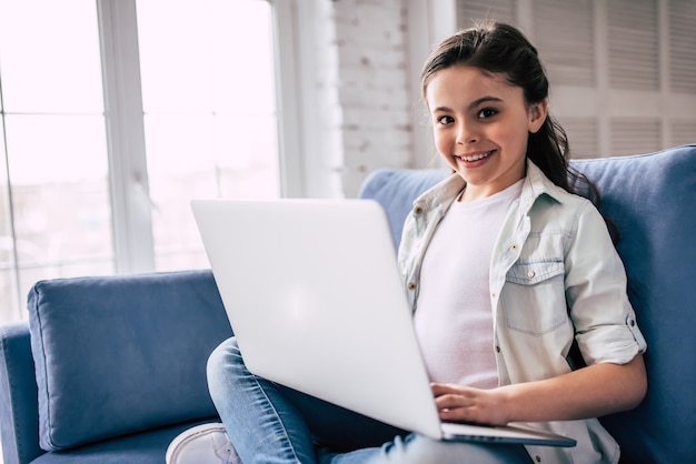 La bambina seduta sul divano con un laptop