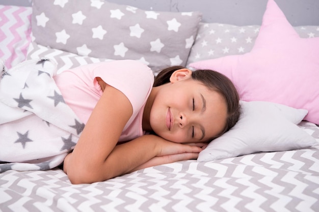 La bambina si addormenta sul cuscino. La qualità del sonno dipende da molti fattori. Scegli un cuscino adatto per dormire bene. La ragazza giaceva sul fondo delle lenzuola del cuscino. Bambino che ha pisolino. Vestiti e cuscini carini.