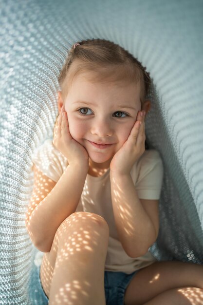 La bambina si diverte sotto il plaid lavorato a maglia blu nella mattina soleggiata