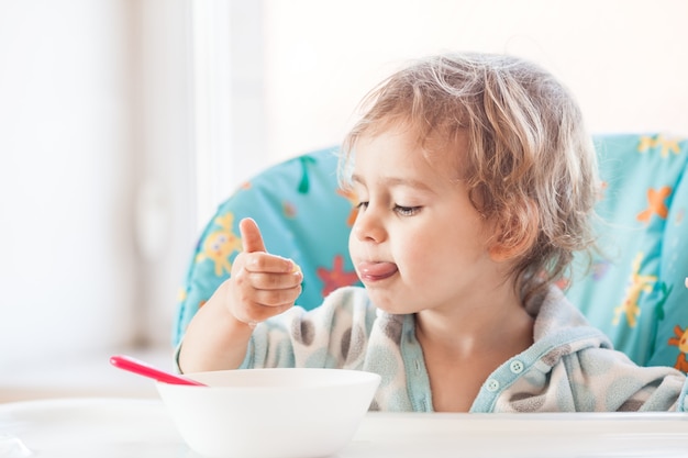 La bambina si siede a un tavolo e mangia con il cucchiaio