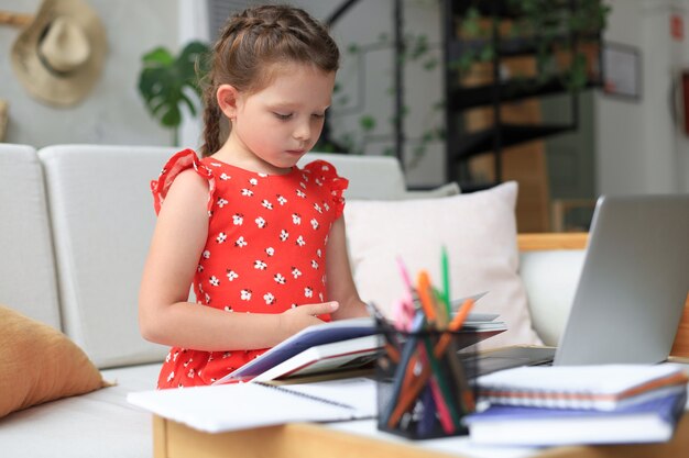 La bambina si siede al desl a casa e fa i compiti, studio personale del materiale, libro di lettura. Il concetto di formazione a distanza