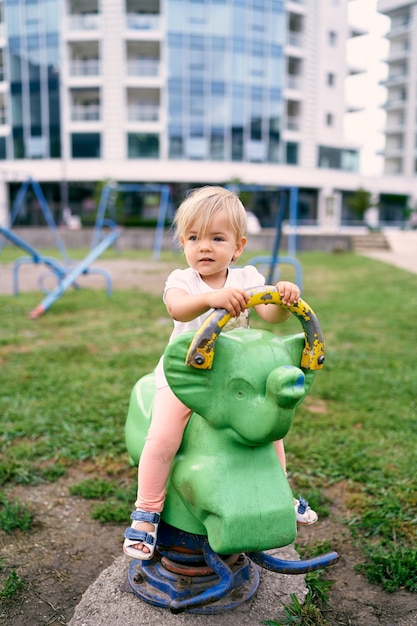 La bambina si siede su un'altalena a molla in un parco giochi nel cortile di un condominio