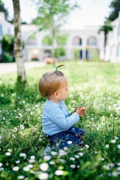 La bambina si siede sulle sue ginocchia sulla vista laterale dell'erba verde