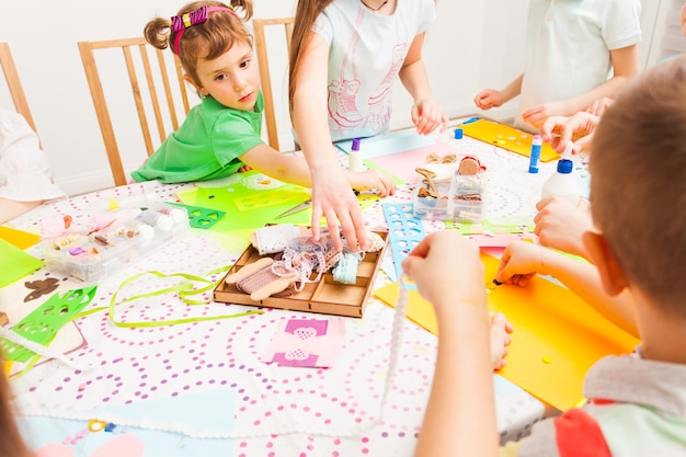 La bambina si siede vicino al tavolo e fa la cartolina insieme ad altri bambini