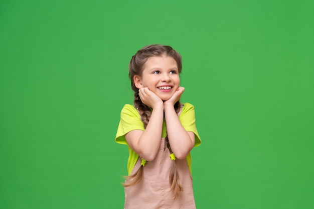 La bambina si stringe le guance e sorride. un bambini con le trecce su uno sfondo verde isolato.