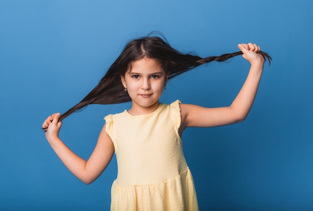 La bambina sorride e tira i suoi lunghi capelli intrecciati isolati su sfondo blu