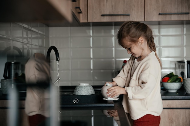 La bambina sorridente aiuta con le faccende domestiche lava i piatti in cucina