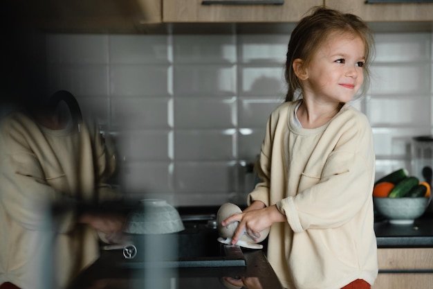 La bambina sorridente aiuta con le faccende domestiche lava i piatti in cucina