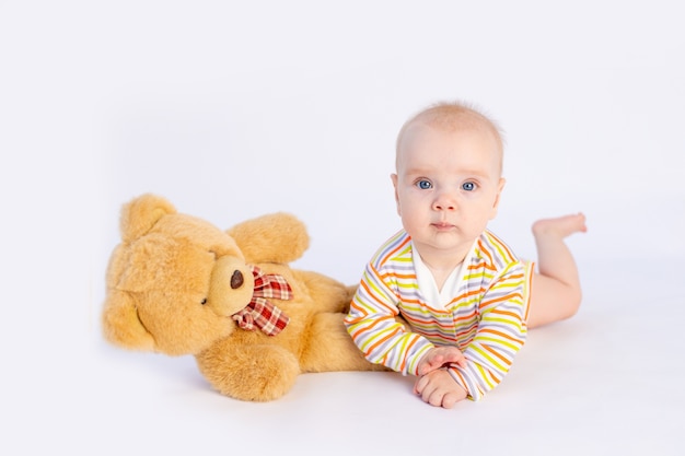 La bambina sorridente di 6 mesi si trova in un body luminoso con un morbido orsacchiotto,