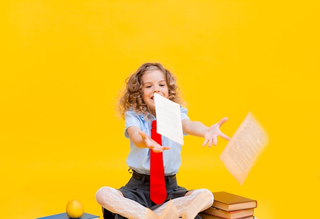 La bambina sorridente felice in un'uniforme scolastica si siede con i libri,