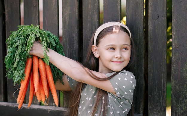 La bambina sorridente in un giardino tiene un mazzo di carote fresche