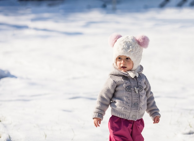La bambina sta camminando al parco innevato in una fredda giornata invernale di sole