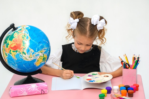 La bambina sta dipingendo con la tempera mentre è seduta al tavolo isolato su bianco