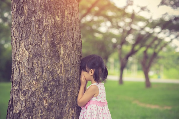 La bambina sta giocando a nascondino nascondino nel parco. Colore vintage