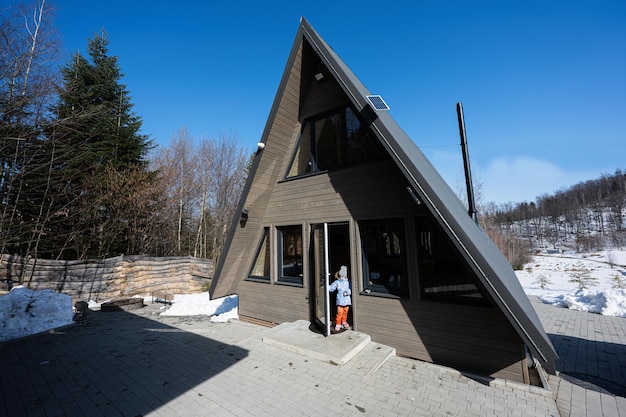 La bambina sta nella porta della piccola casa di cabina del paese del triangolo in montagna