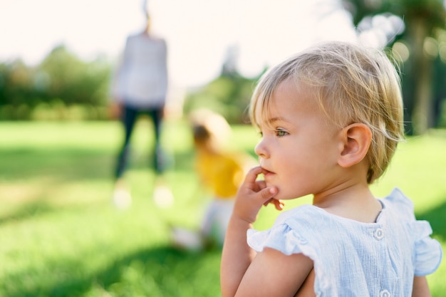 La bambina sta su un prato verde girandosi di lato con un dito in bocca ritratto