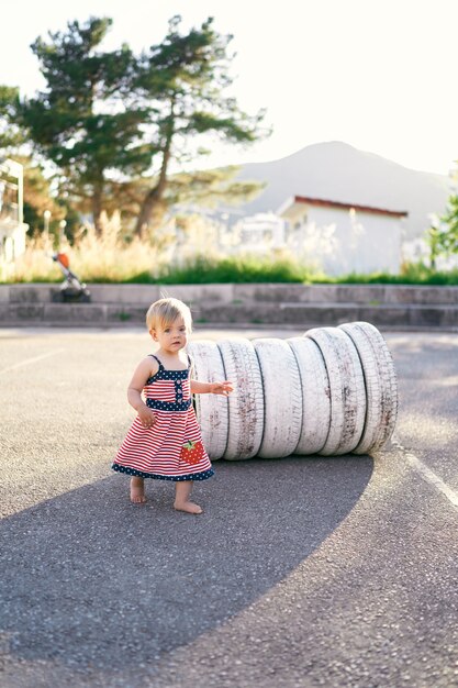 La bambina sta vicino alle gomme bianche nel parcheggio